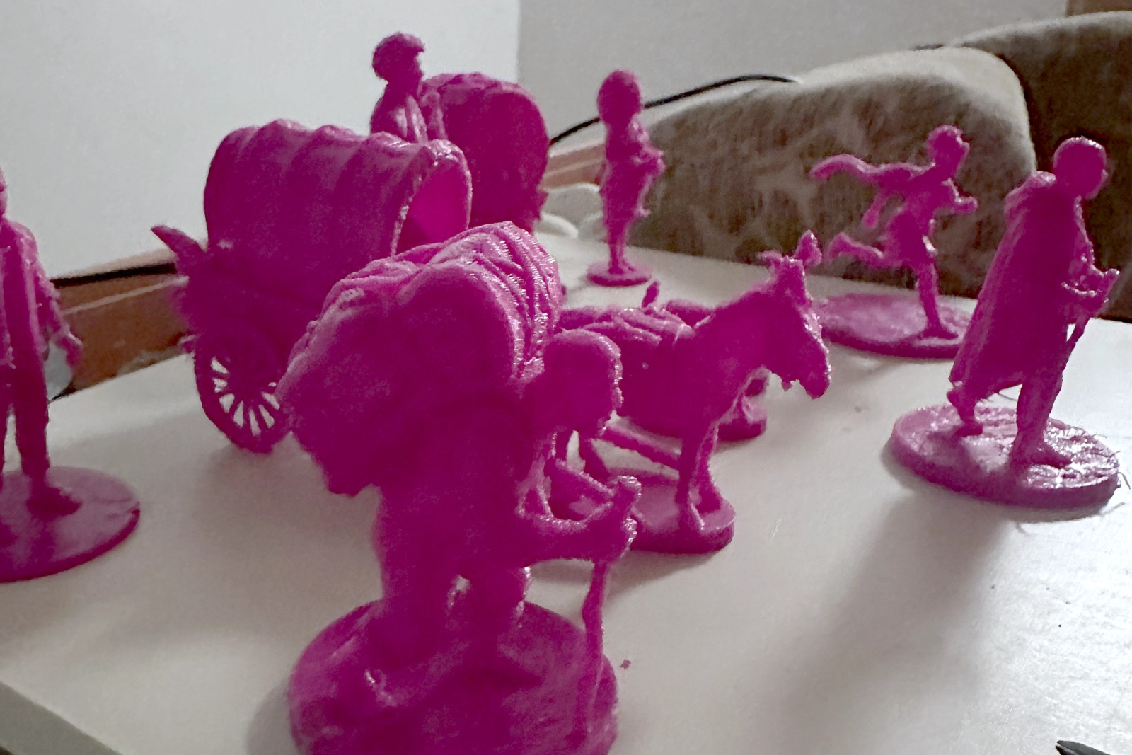 Magenta 3D-printed figures on a desk: a covered caravan, a donkey and several travellers.