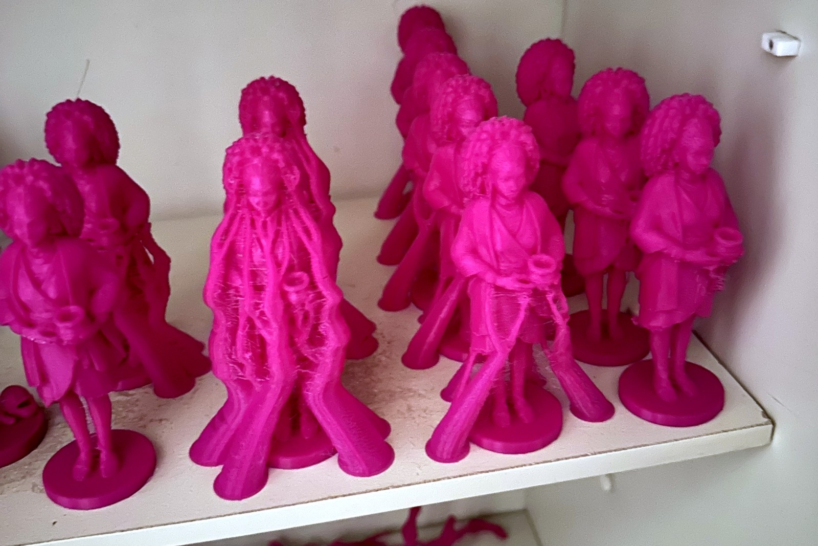 Several magenta 3D-printed Amara figurines, 120 mm tall, standing on a shelf; some still carry support trees.
