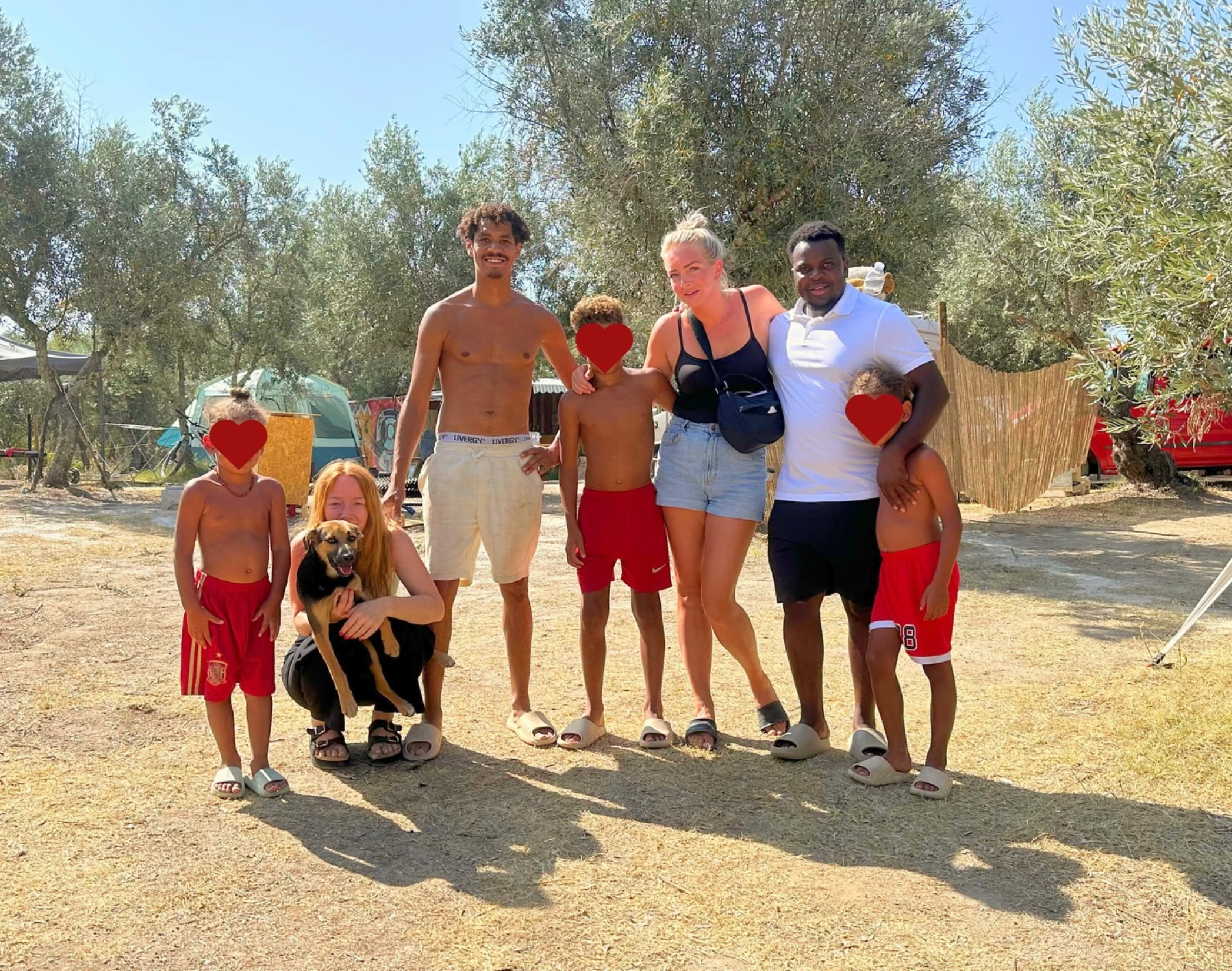 A group of guests at the off-grid camp in an olive grove, tents behind them; the children’s faces are covered with hearts.